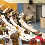 University classroom with students and professor at podium.